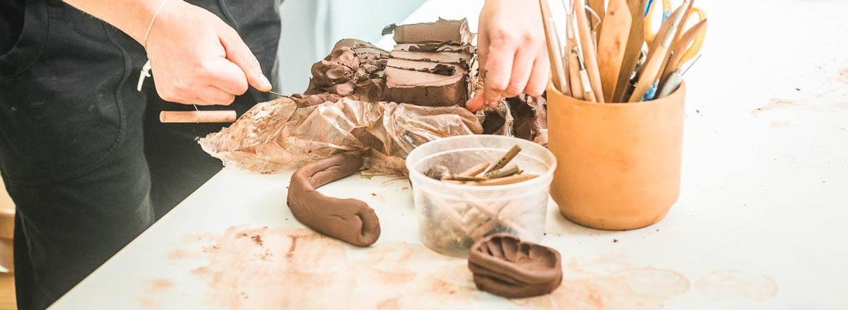 Na zdjęciu: dłoń nad stołem z akcesoriami do prac ceramicznych. Fot. SDK